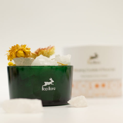 Clear quartz and dried flower vessel with yellow flowers, its cream box blurred behind