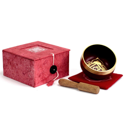 Root chakra singing bowl and wooden striker beside the red cushion and open bowl box