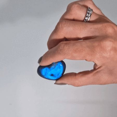 Hand holding a labradorite heart-shaped stone with a bright blue flash