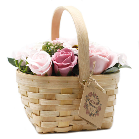 Pink soap flowers in a wicker basket with a tall handle and hanging tag, shown close up on white