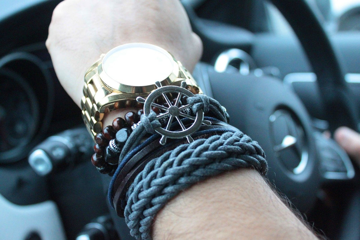 A wrist wearing several bracelets and a gold watch inside a car.