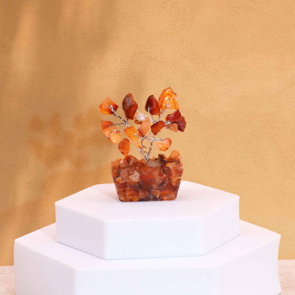 A small carnelian gemstone tree on a white stepped pedestal against a gold background.
