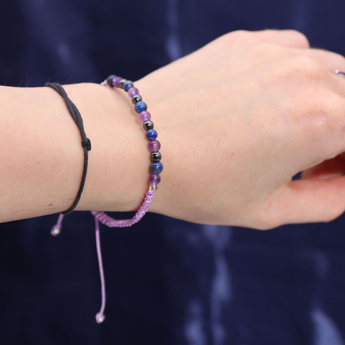 A hand wearing a beaded bracelet and a black cord bracelet against a dark background.