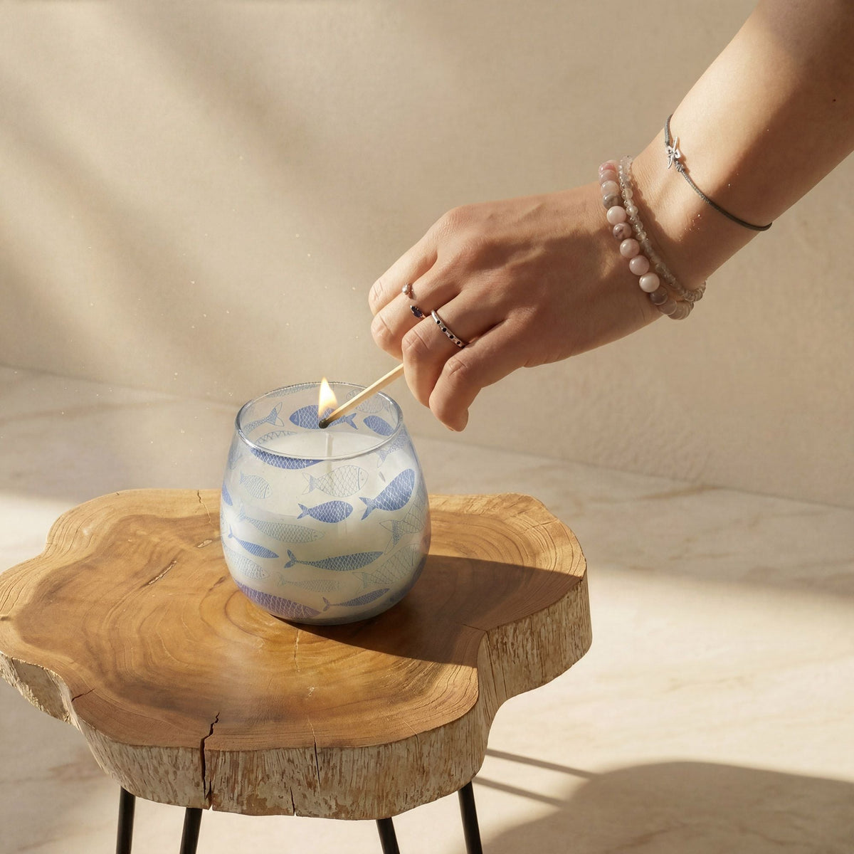 A hand lights a glass jar candle on a wooden table.