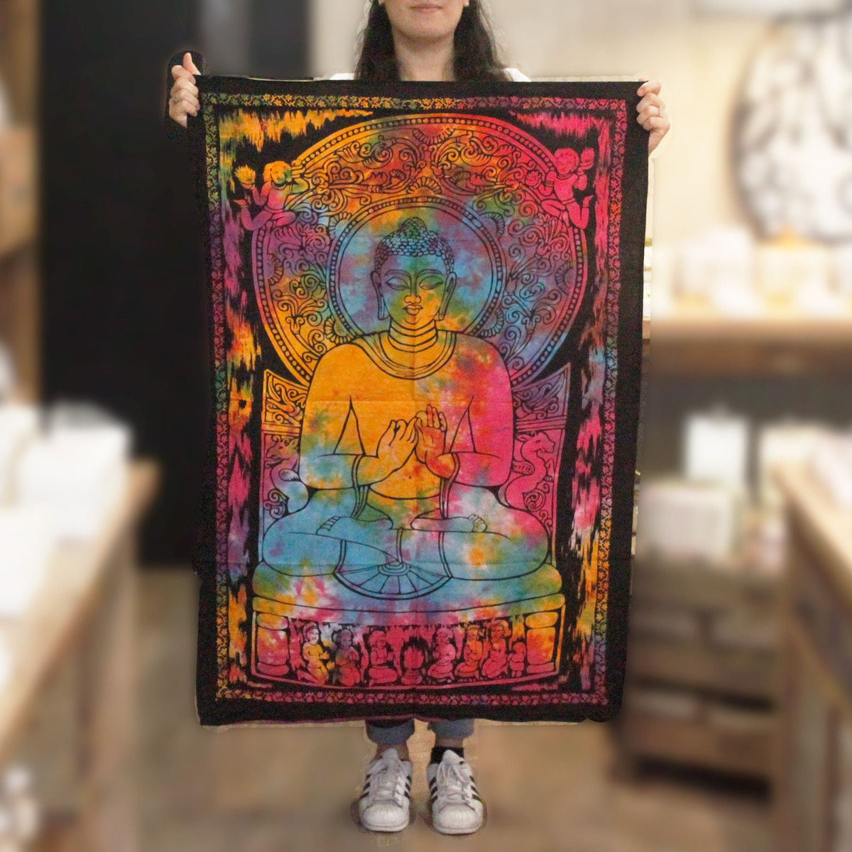 A person holds up a colourful Buddha wall hanging with a black border.
