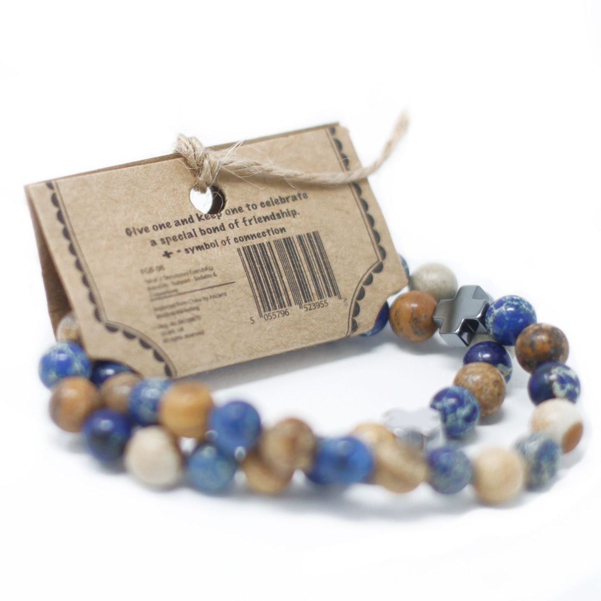 Two beaded friendship bracelets in front of a small brown cardboard gift tag with twine on a white background.