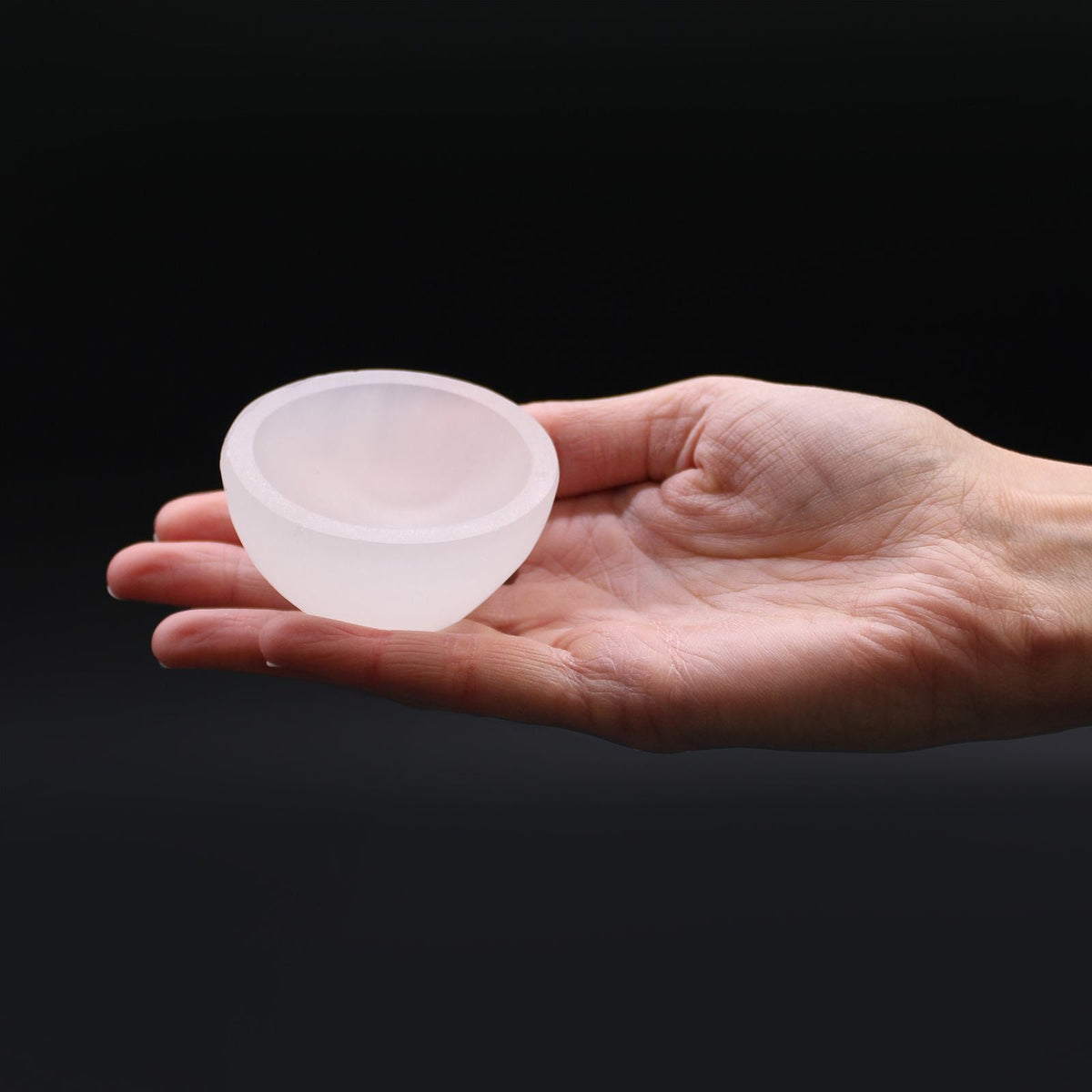 A small frosted white bowl resting on an open hand against a black background.