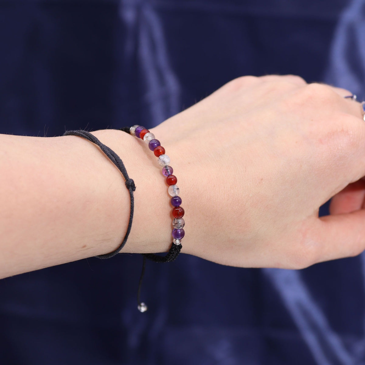 A hand wearing two beaded bracelets against a dark blue background.