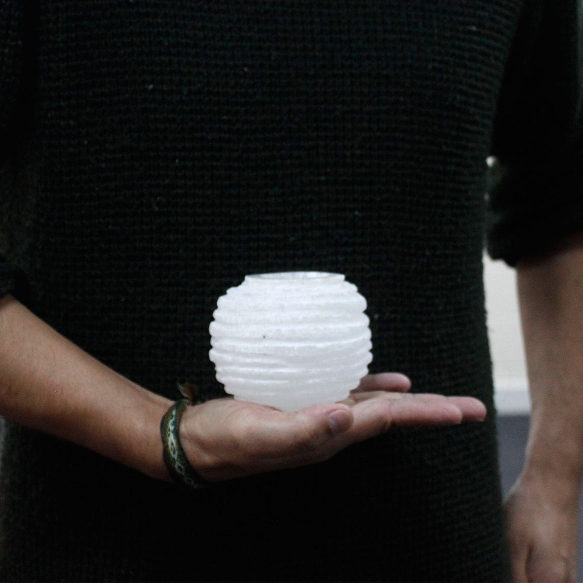 A person holding a small white ribbed candle holder in one hand.