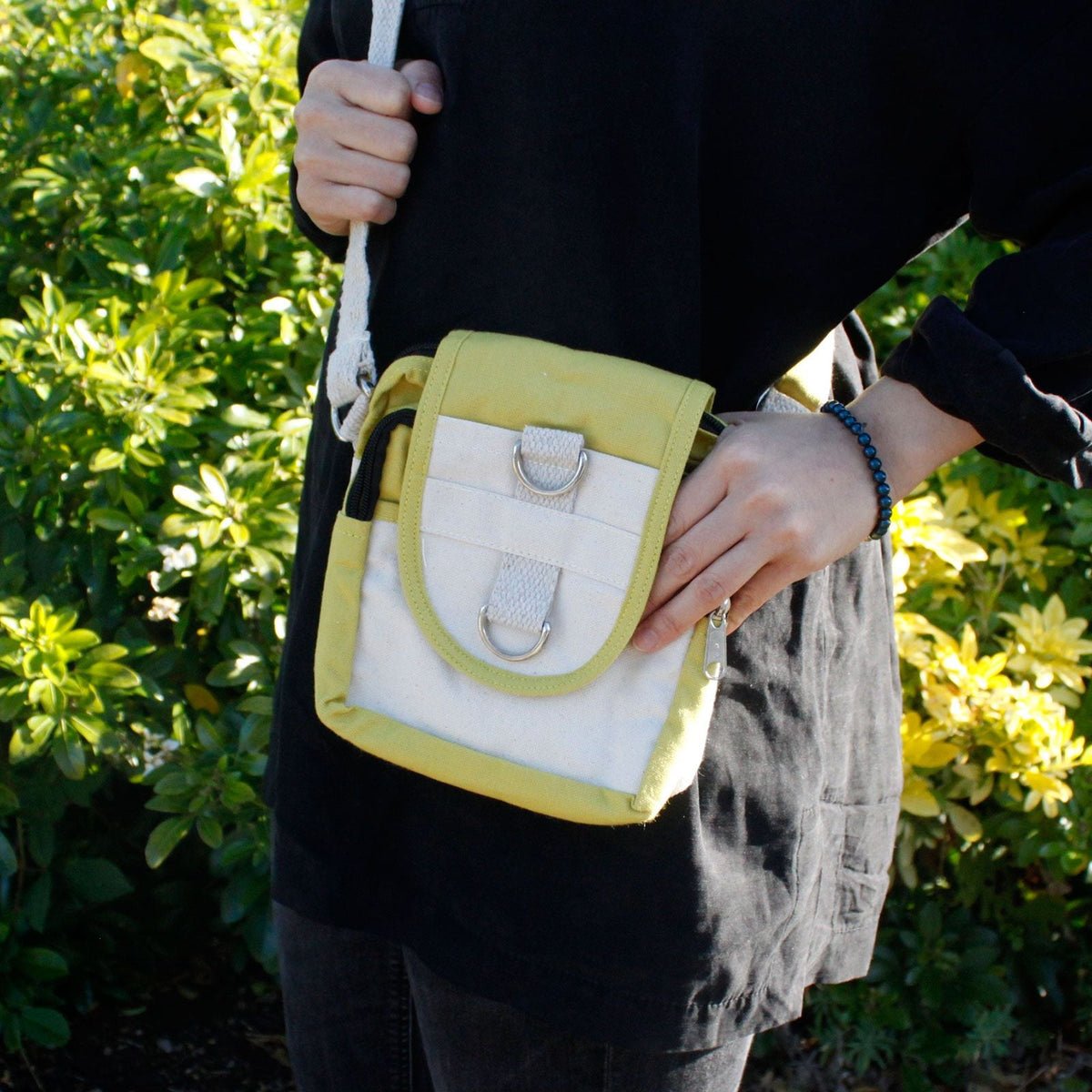 A person holding a small cream and olive crossbody bag outdoors.