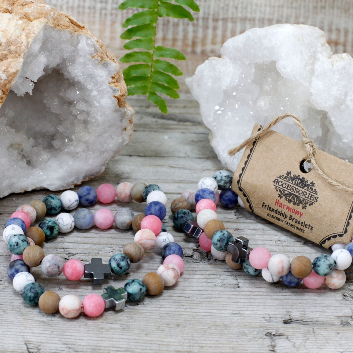 Two beaded friendship bracelets on a wooden surface beside a tagged label and two white crystal rocks.