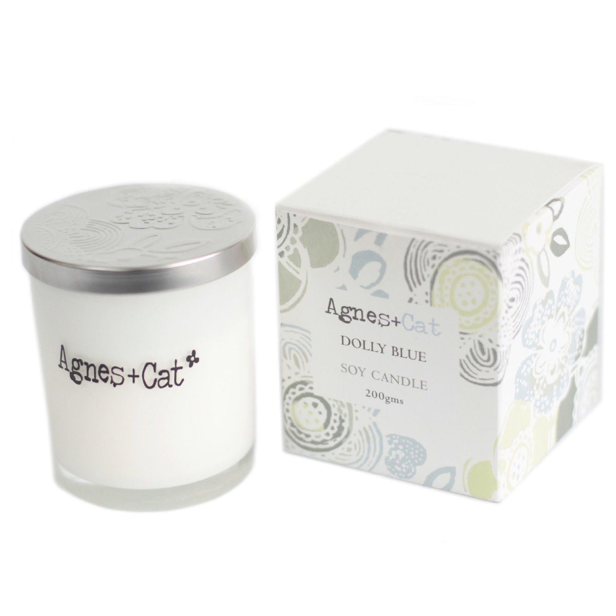 A white candle in a glass jar with a metal lid beside its patterned box.