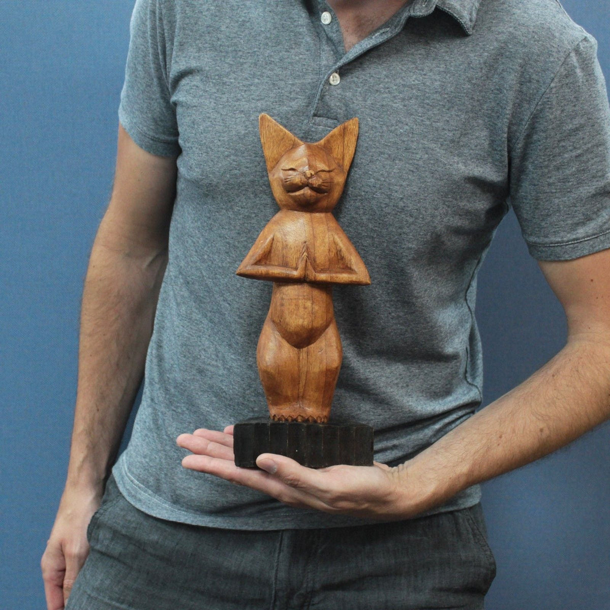 A person holding a carved wooden cat figurine on a black base.