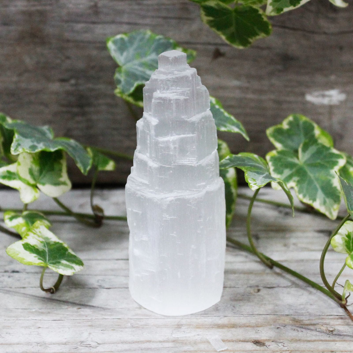 A white carved tower-shaped crystal on a grey wooden surface, surrounded by green ivy leaves.