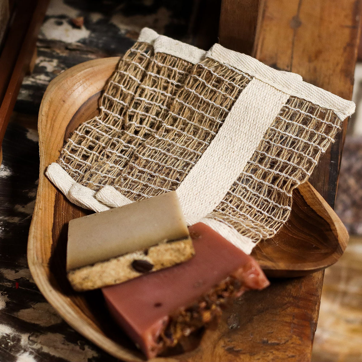 A jute soap bag in a wooden dish, with two soap bars in front.