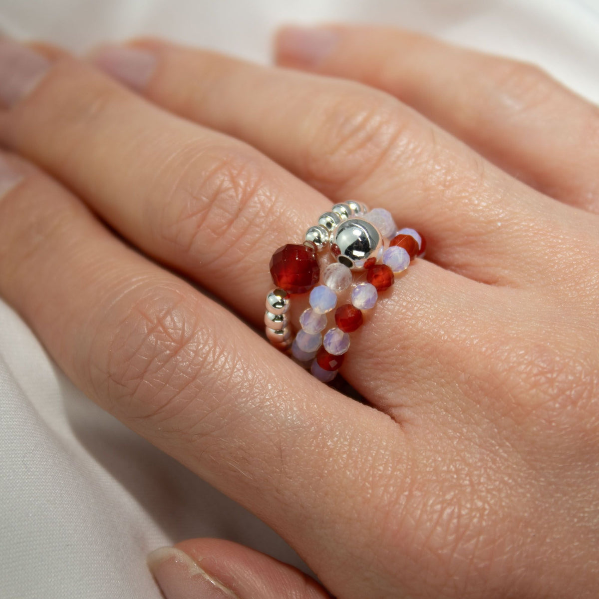 A hand wearing several beaded rings with red, clear and pale purple beads.