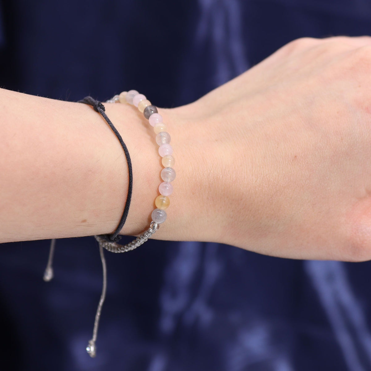 A hand and wrist wearing two beaded bracelets against a dark blue background.
