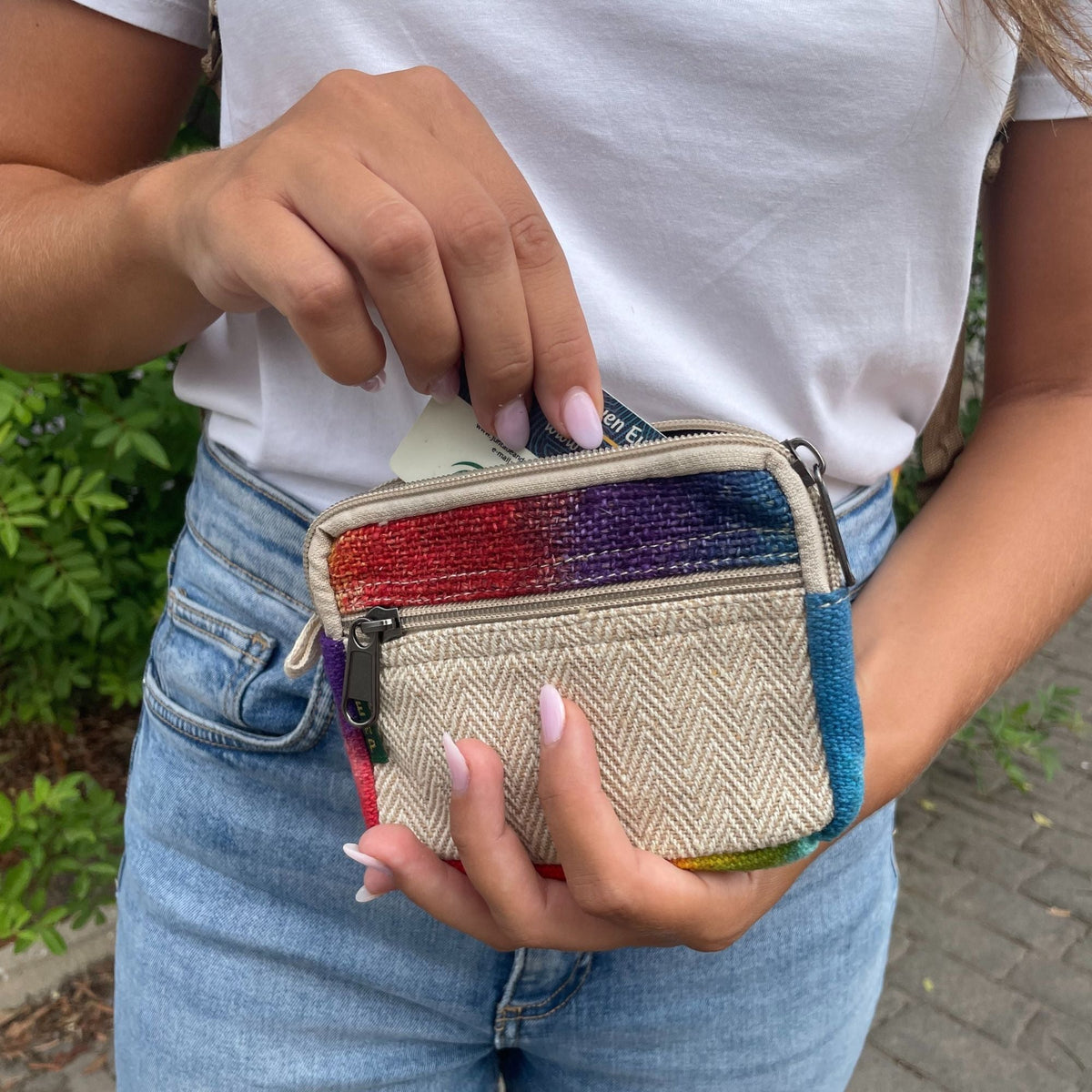 A person holding a small square zip pouch with a rainbow top and beige front panel.