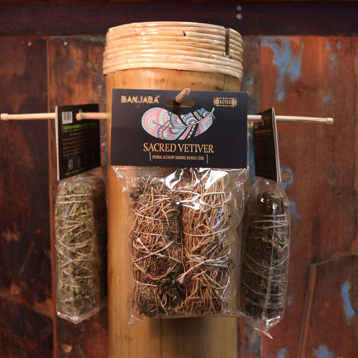 Three bundles of dried herbs hanging in clear plastic bags around a bamboo container.