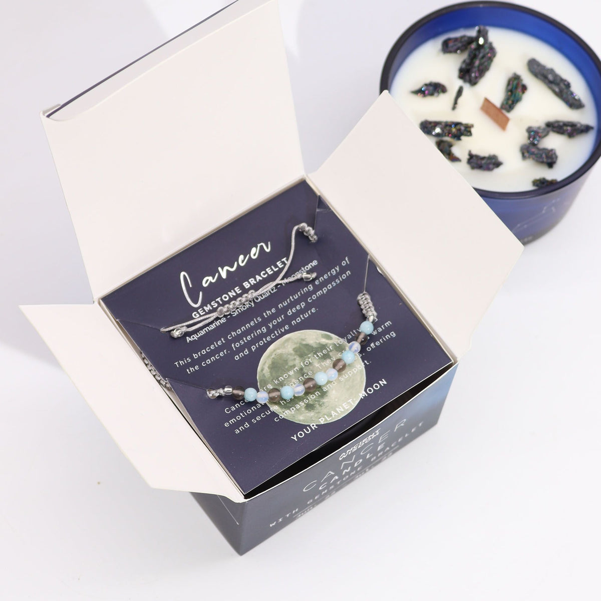 An open candle box with a Cancer gemstone bracelet inside, beside a blue candle in a tin.