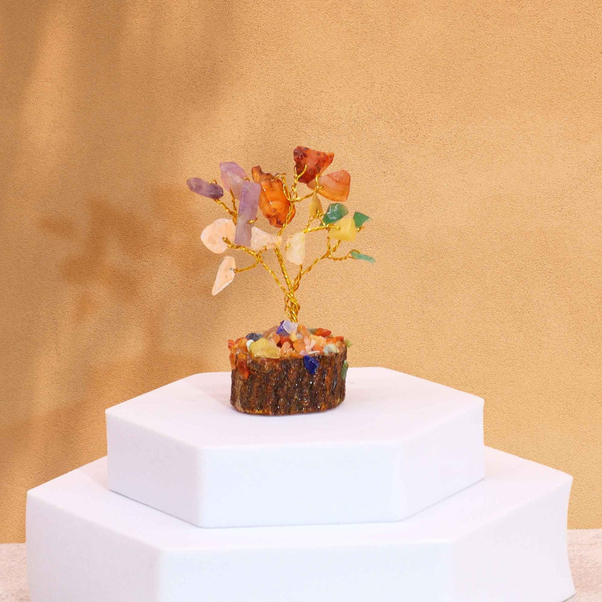 Small gemstone tree with multicoloured stones on a round wooden base, set on white stepped blocks.