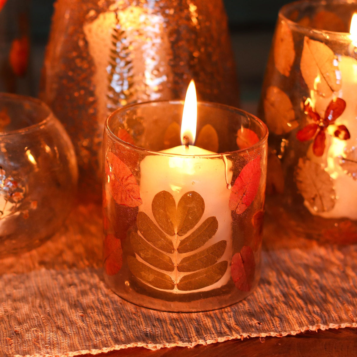 A lit candle in a floral glass holder, with other candle holders around it on a table.