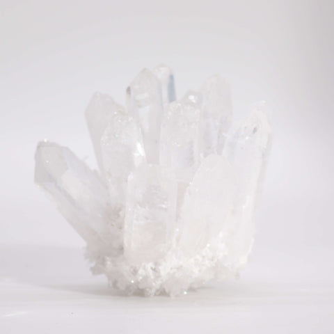 Clear quartz cluster standing upright on a plain white surface, shown from the front