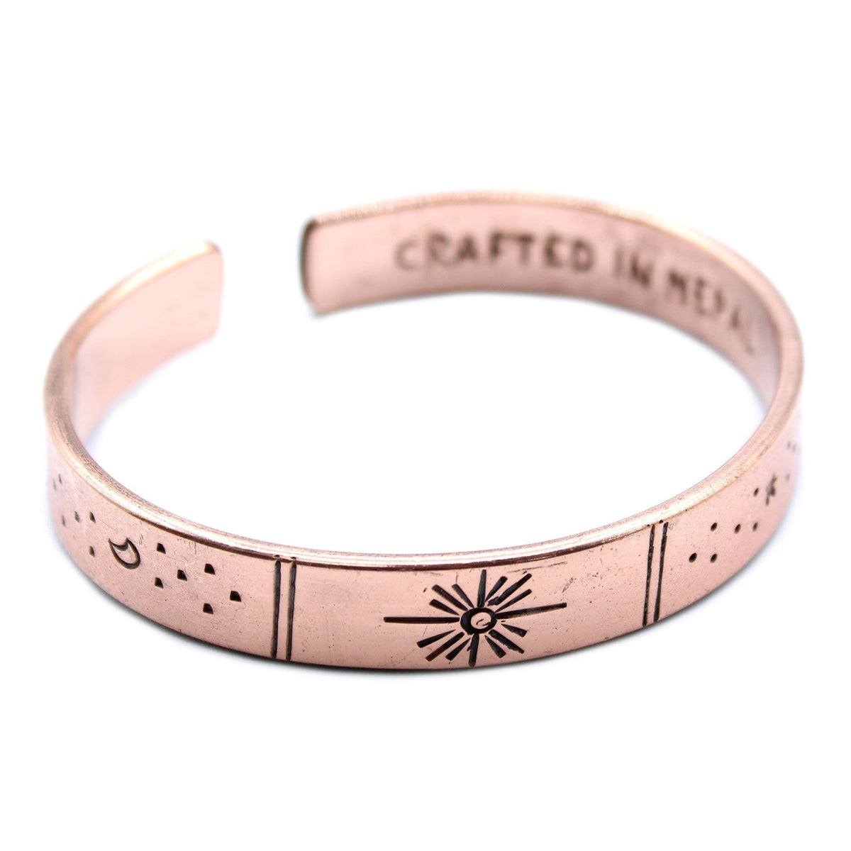 Close view of the open copper cuff, showing its sun, moon and star markings against a white background