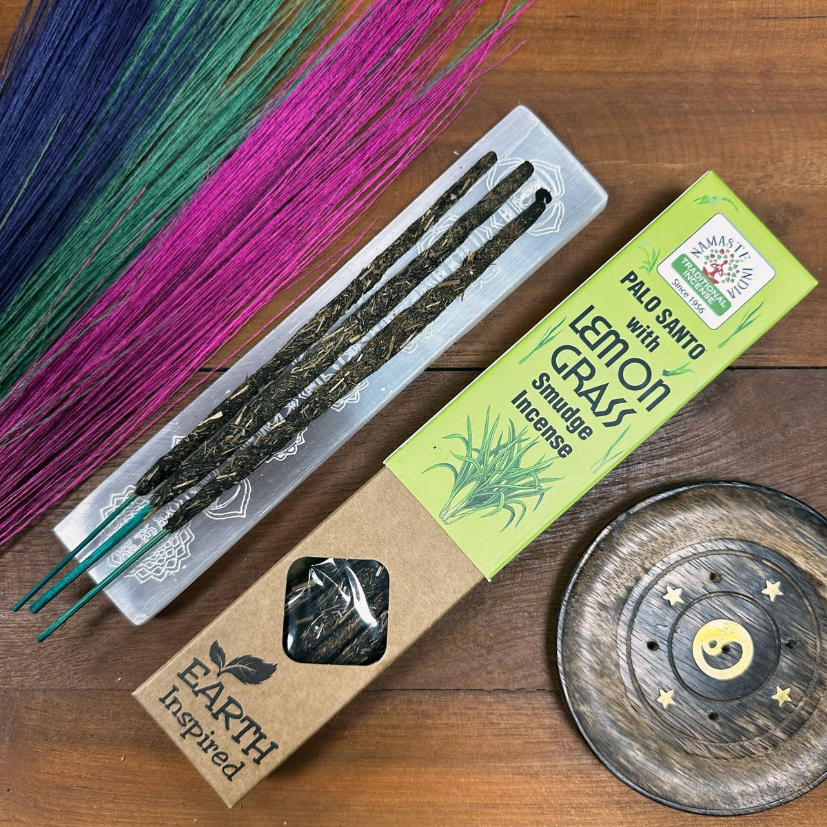 Lemon Grass smudge incense sticks fanned out on a metal tray beside a round incense burner