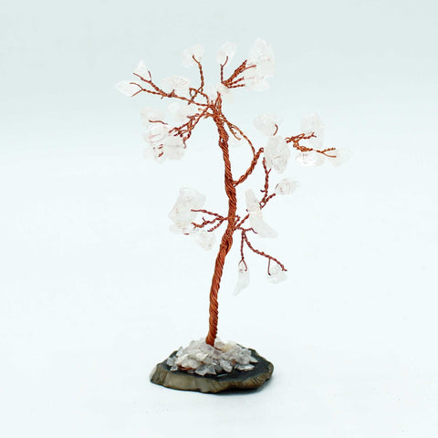 Rock quartz gemstone tree shown alone on its black agate base against a pale background