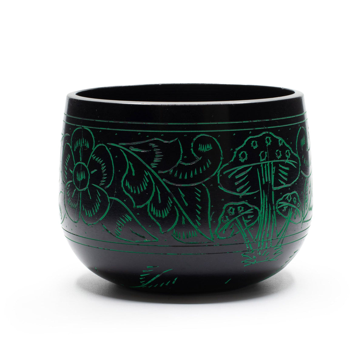 Green singing bowl standing on a white surface, with mushroom and foliage engravings across the front