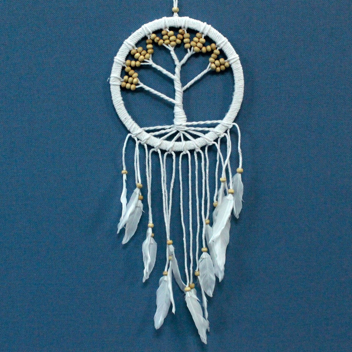 White Tree of Life dreamcatcher with tan beads and feathers, hanging against a blue background