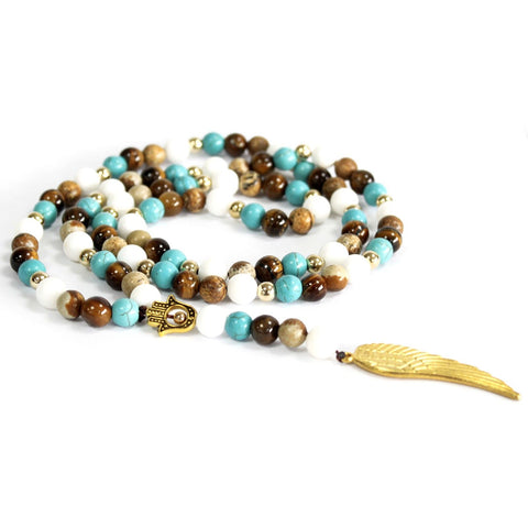 Multi-bead necklace in turquoise, white and brown, coiled on white with a gold wing pendant
