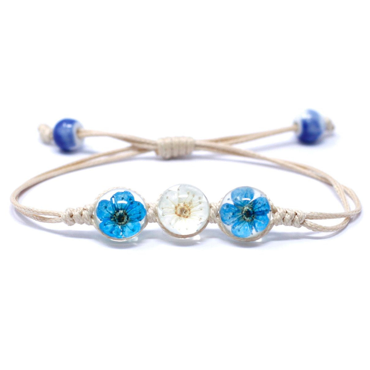 Close-up of the bracelet front with three blue and white flower charms on a pale cord