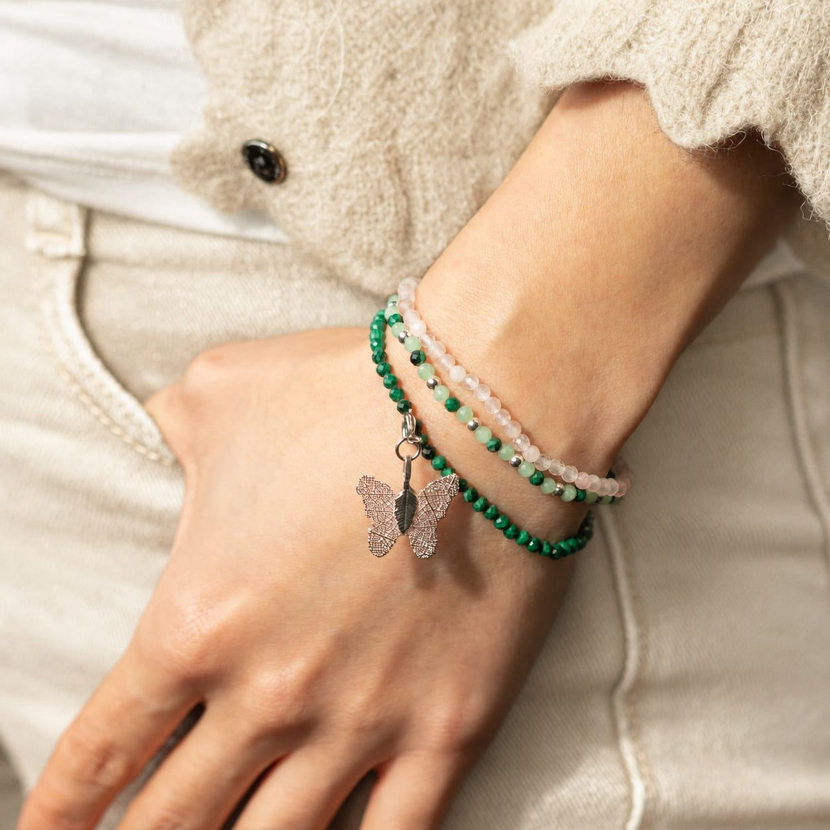 Bracelets worn on a wrist beside a cream sleeve