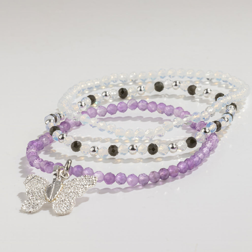 Three purple, pale and dark beaded bracelets with a butterfly charm