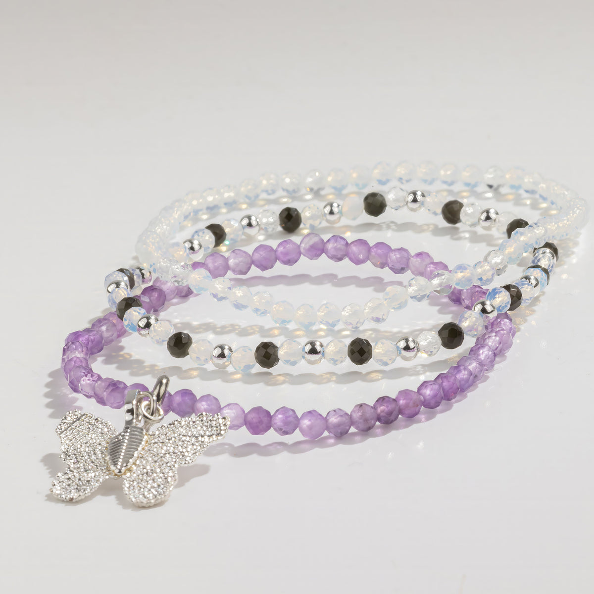 Three purple, pale and dark beaded bracelets with a butterfly charm