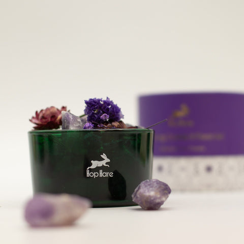 Green glass vessel with amethyst chunks and purple and red dried flowers, box blurred behind
