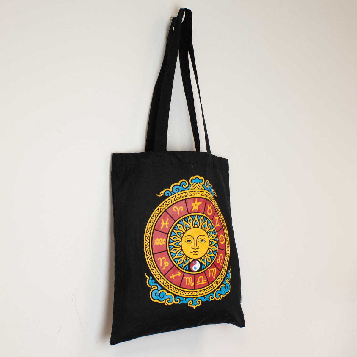 Iconic Classic Tote Bag, Zodiac Sun, Black 6oz, hanging against a pale wall, front view