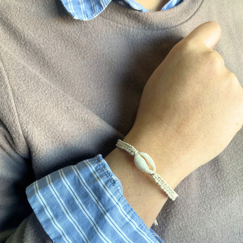 Handmade Friendship Bracelet with a white cowrie shell worn on a wrist, close-up with blue striped sleeves