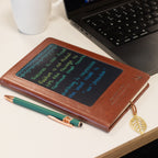 Brown notebook with writing on its screen, beside a pen