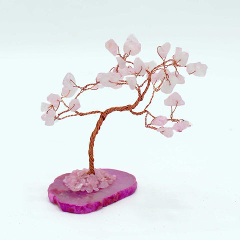 Rose quartz tree shown from the side, with its pink agate base on a white surface