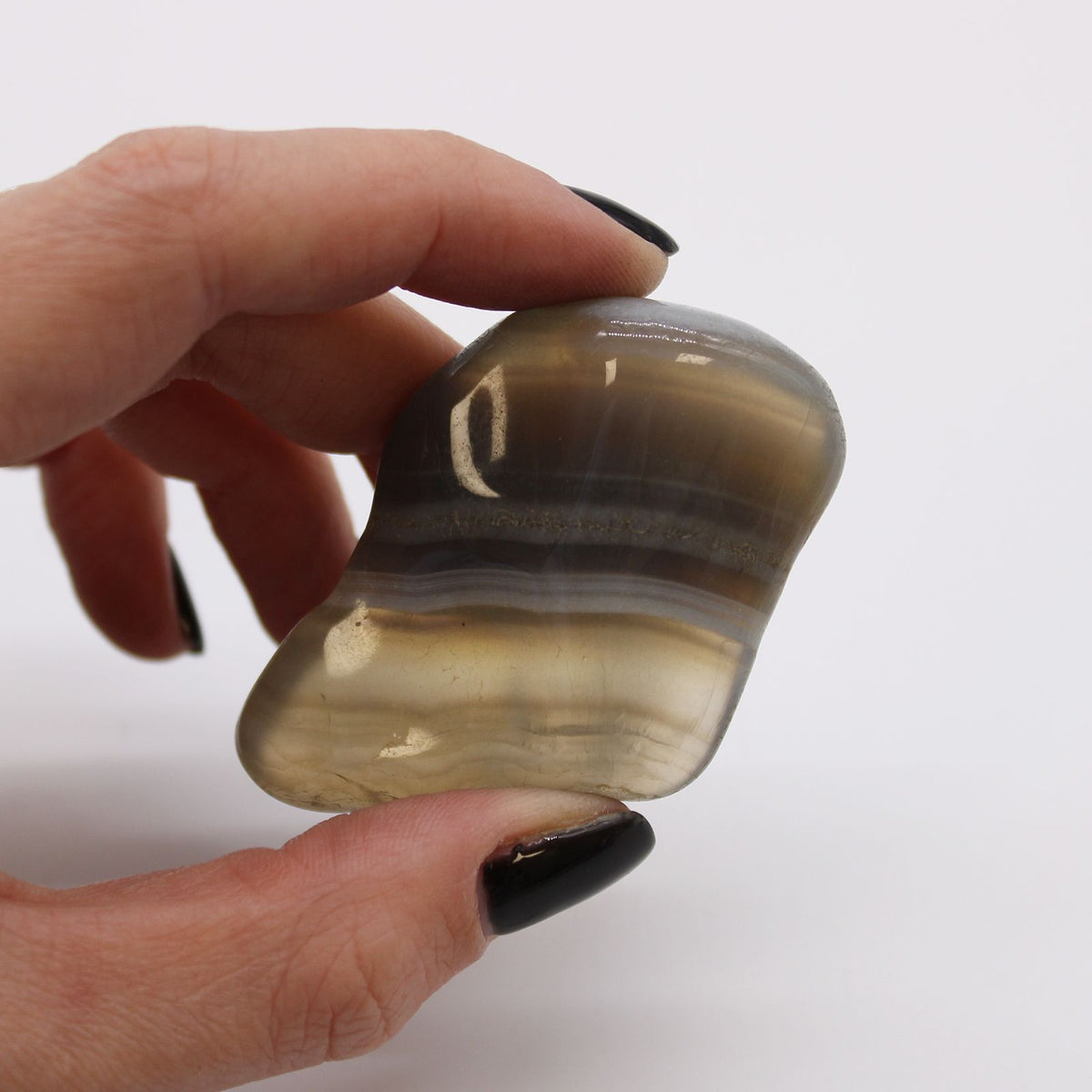 Large African Tumble Stone, grey and cream banded agate held between fingers in close-up