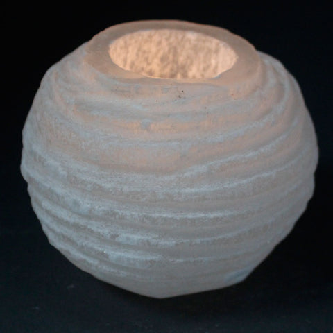 Snowball candle holder in a close-up against a dark background, showing its pale ridged sides and open top