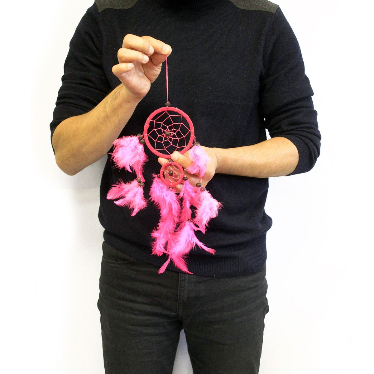 Bali Dreamcatchers, a bright pink round web with dangling feathers, held against a black jumper