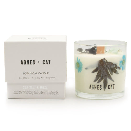 Agnes + Cat Sea Salt and Moss soy candle in a glass jar with dried florals set in the wax, beside its box.