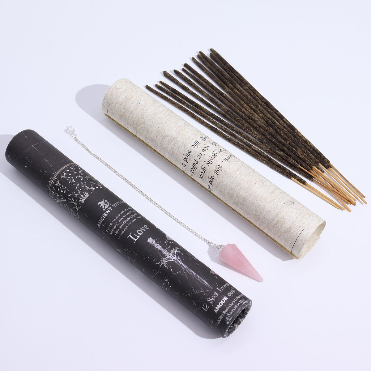 Love spell incense tube with its pale outer tube, incense sticks and pink pendulum laid out on white