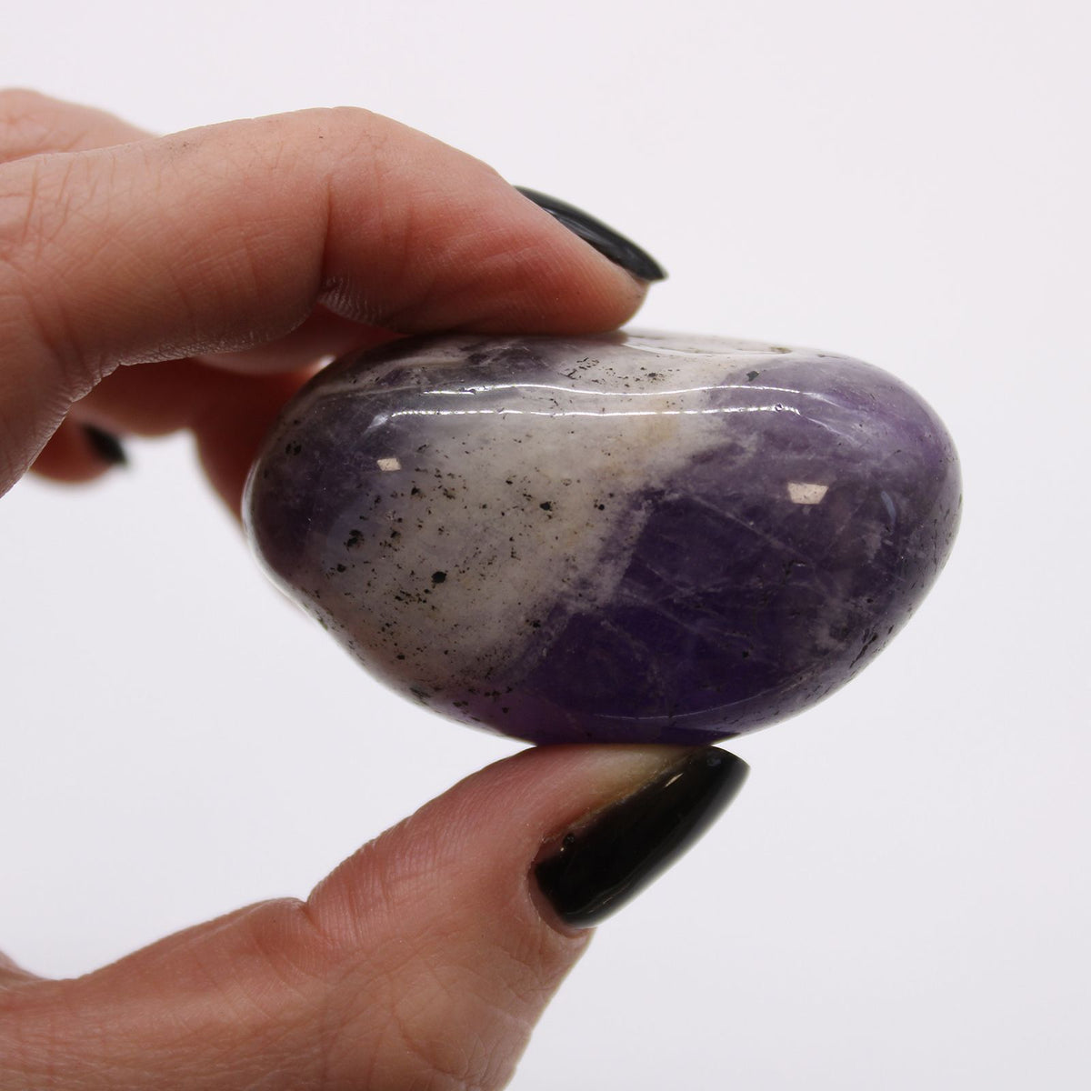 Large African Tumble Stones, Amethyst, a polished purple and pale stone held between fingers