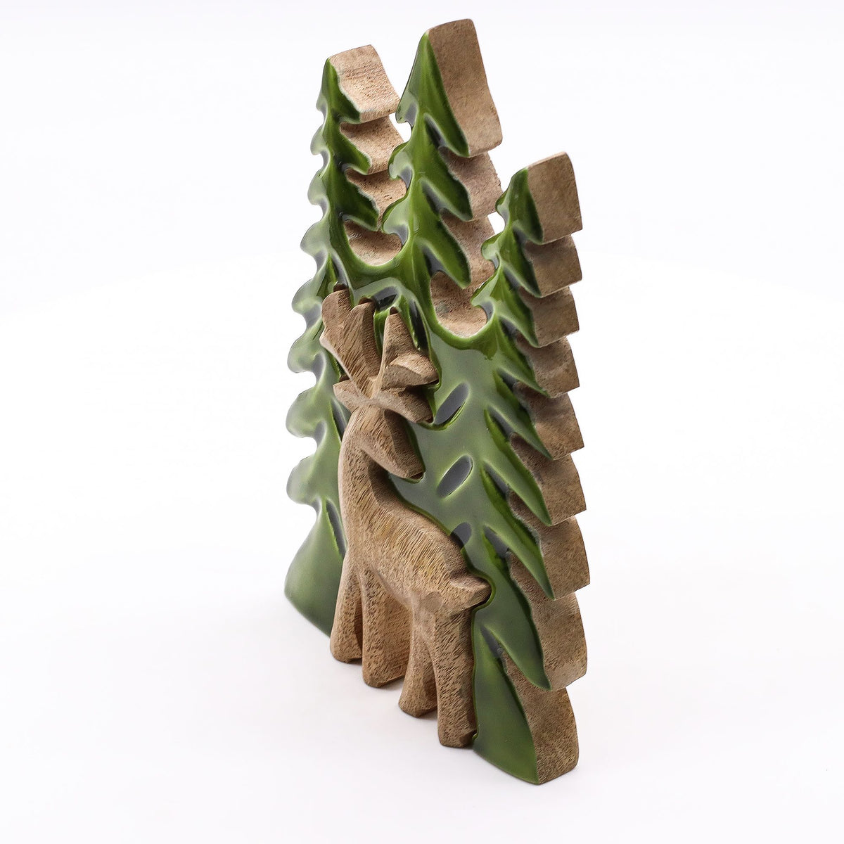 Angled view of a mango wood reclining stag among green-enamelled layered pine trees