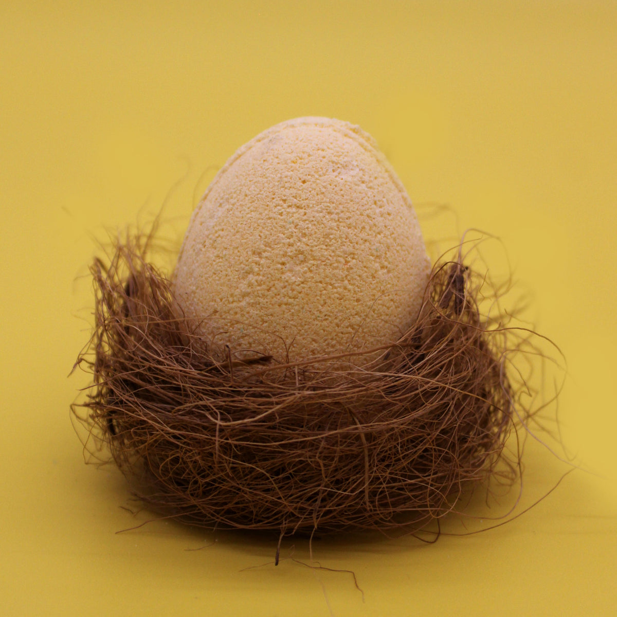 6 Bath Eggs in a Tray, Banana, one pale peach egg nestled in brown fibres against a yellow background